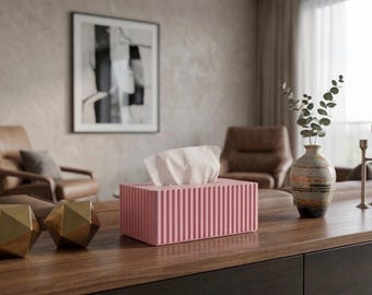 Könnte beinhalten: Eine rosa rechteckige Taschentuchbox mit vertikalen Linien, die weiße Taschentücher enthält. Die Box steht auf einer dunklen Holzoberfläche, neben goldenen geometrischen Dekorationen und einer Vase mit Grün. Der Raum hat eine neutrale Farbpalette.