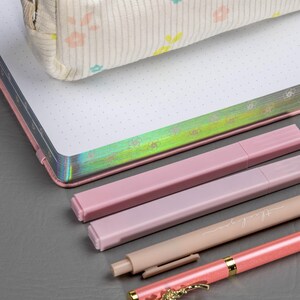 May include: A stationery set featuring a floral-patterned pencil case, a dot grid notebook, and several pink pens. One pen has the words "thank you" printed on it, and another has a decorative floral design.