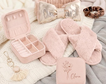 May include: A collection of pink accessories including a jewelry box, headband with "OMG! OMG!" text, slippers, scrunchie, keychain, and a small box with floral design and the name "Olivia". The items are arranged on a white and gray blanket.