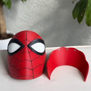 May include: A red and black Spider-Man mask with white eye lenses and a separate red face shield. The mask features a web pattern and is likely made of plastic or a similar material.