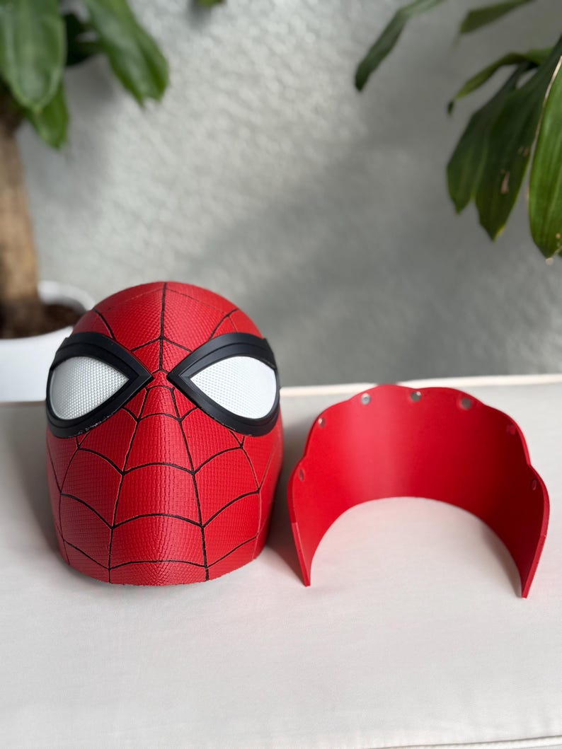May include: A red and black Spider-Man mask with white eye lenses and a separate red face shield. The mask features a web pattern and is likely made of plastic or a similar material.