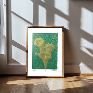 Puede incluir: Una impresión artística enmarcada con una ilustración botánica de calas. La obra de arte presenta tonos verdes y dorados con una representación detallada de las flores sobre un fondo verde. La impresión se presenta en un marco de madera.