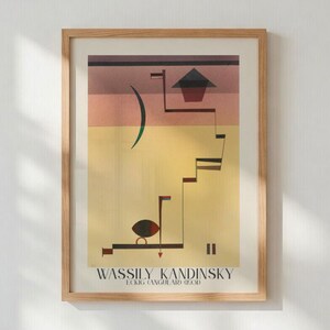May include: Framed print of Wassily Kandinsky's "Eckig (Angular) (1930)". The artwork features geometric shapes and lines in shades of red, yellow, and brown. The print is encased in a light brown wooden frame.