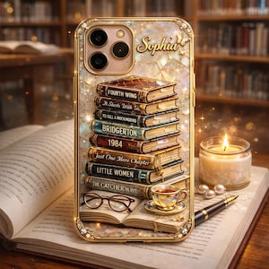 Könnte beinhalten: Goldfarbene Handyhülle mit einem Bücherstapel, darunter "Fourth Wing" und "1984". Die Hülle hat einen marmorartigen Hintergrund und den Namen "Sophia". Eine Teetasse, eine Brille und ein Stift sind ebenfalls zu sehen.