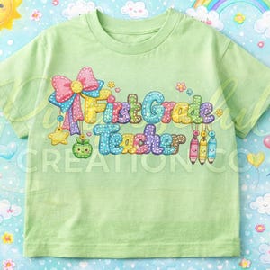 Può includere: Maglietta verde chiaro con la scritta "First Grade Teacher" in lettere colorate e cucite. Il design include un fiocco, stelle, una mela e matite. Lo sfondo presenta un motivo stravagante di arcobaleni, nuvole e cuori.