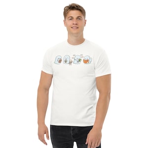 May include: A white short-sleeved t-shirt featuring a graphic print of four light blue ghosts. The ghosts are depicted performing various activities, including writing on a clipboard, holding a drink, waving, and reading an orange book.