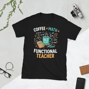 Può includere: Una t-shirt nera a maniche corte con una grafica che riporta il testo COFFEE + MATH = FUNCTIONAL TEACHER. Il design include una tazza da caffè color verde acqua, una calcolatrice arancione e vari simboli e formule matematiche in bianco.