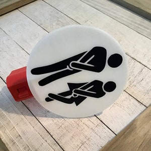 May include: White round light switch cover with a black silhouette of two people sitting side by side. The people are facing the same direction.
