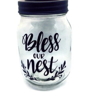 May include: A clear glass jar with a black lid and a black vinyl decal that says "Bless our nest".