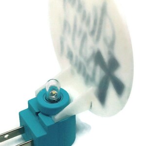 May include: A teal blue night light plug-in with a white plastic shade. The shade has a design on it that is difficult to read. The night light has a small white light bulb.