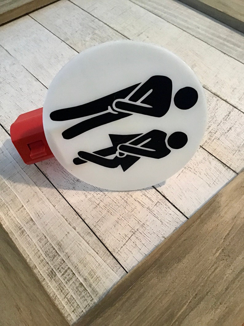 May include: White round light switch cover with a black silhouette of two people sitting side by side. The people are facing the same direction.