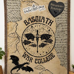 Puede incluir: Una manta beige con un dise&ntilde;o de drag&oacute;n negro y texto. La manta presenta las palabras "BASGIATH WAR COLLEGE" en un dise&ntilde;o circular, junto con la frase "you're really a violent little thing aren't you?" y un dise&ntilde;o en forma de coraz&oacute;n que dice "Shadow Naddy".