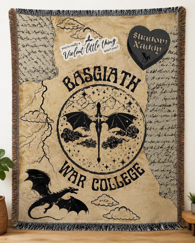 Puede incluir: Una manta beige con un dise&ntilde;o de drag&oacute;n negro y texto. La manta presenta las palabras "BASGIATH WAR COLLEGE" en un dise&ntilde;o circular, junto con la frase "you're really a violent little thing aren't you?" y un dise&ntilde;o en forma de coraz&oacute;n que dice "Shadow Naddy".