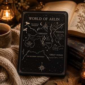 May include: A rectangular black metal tin featuring a gold-toned map titled World of Aelin. The map displays geographical labels including The Witch Kingdom, Terrasen, Wendlyn, The Deserted Lands, Eylkwe, The Southern Continent, and Great Ocean.