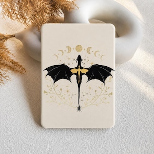 Puede incluir: Una funda rectangular para tableta de color crema con una silueta de dragón negra central y detalles dorados. El diseño incluye un ciclo de fases lunares dorado sobre el dragón, rodeado de delicadas estrellas doradas y finas enredaderas.
