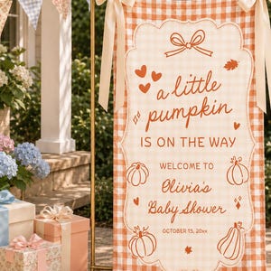 Puede incluir: Una pancarta de tela rectangular vertical con un patrón de cuadros vichy naranja y blanco, que presenta el texto "a little pumpkin IS ON THE WAY" y "WELCOME TO Olivia's Baby Shower OCTOBER 15, 20xx" con ilustraciones de calabazas, corazones y hojas.