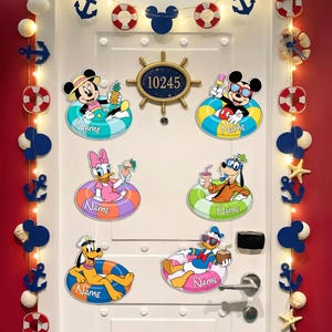 May include: A white door decorated with Disney character cutouts in inner tubes. Mickey Mouse, Minnie Mouse, Donald Duck, Daisy Duck, Goofy, and Pluto are featured. The door also has nautical-themed decorations like anchors and life preservers.