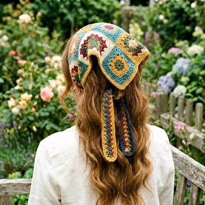 May include: A vibrant, crocheted headscarf with a patchwork design. The scarf features squares of teal, yellow, burgundy, and cream. Long, decorative ties hang down the back. The head covering is worn over long, wavy brown hair.