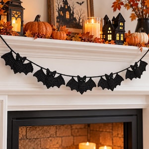 May include: A black crochet bat garland featuring five individual bat-shaped ornaments strung together on a matching black yarn cord. Each bat has a textured, hand-stitched appearance with small, round, dark eyes and outstretched wings.