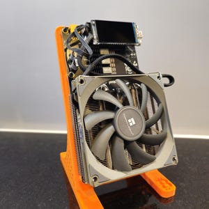 Peut inclure: Un refroidisseur de processeur d'ordinateur avec un grand ventilateur et un dissipateur thermique, monté sur un support orange. Le ventilateur est gris avec des pales noires et un cadre argenté. Le support est en plastique orange.