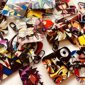 Könnte beinhalten: Eine Sammlung von Schlüsselanhängern mit abstrakter Kunst und schwarzen Metallverschlüssen. Die Schlüsselanhänger weisen geometrische Designs in verschiedenen Farben auf, darunter Rot, Blau, Gelb und Schwarz. Der Kunststil erinnert an den Kubismus und die moderne Kunst.
