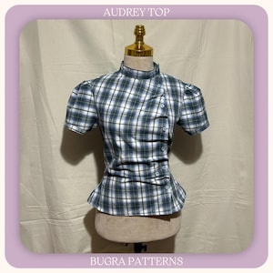 May include: A short-sleeved top with a high neckline and a blue, white, and green plaid pattern. The garment features an asymmetrical button placket running diagonally down the front with gathered fabric details. The text AUDREY TOP and BUGRA PATTERNS is visible.