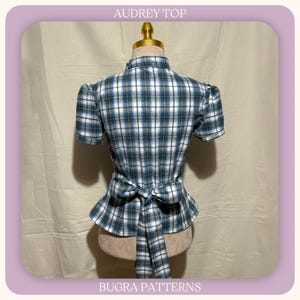 May include: A short-sleeved top with a blue, green, and white plaid pattern, featuring a high collar, puffed sleeves, and a tie-waist detail at the back. The text AUDREY TOP and BUGRA PATTERNS is printed at the top and bottom of the image frame.