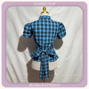 May include: A short-sleeved top with a blue and black plaid pattern, featuring a high collar, puff sleeves, and a tie-waist detail at the back. The text AUDREY TOP and BUGRA PATTERNS is visible at the top and bottom of the image frame.