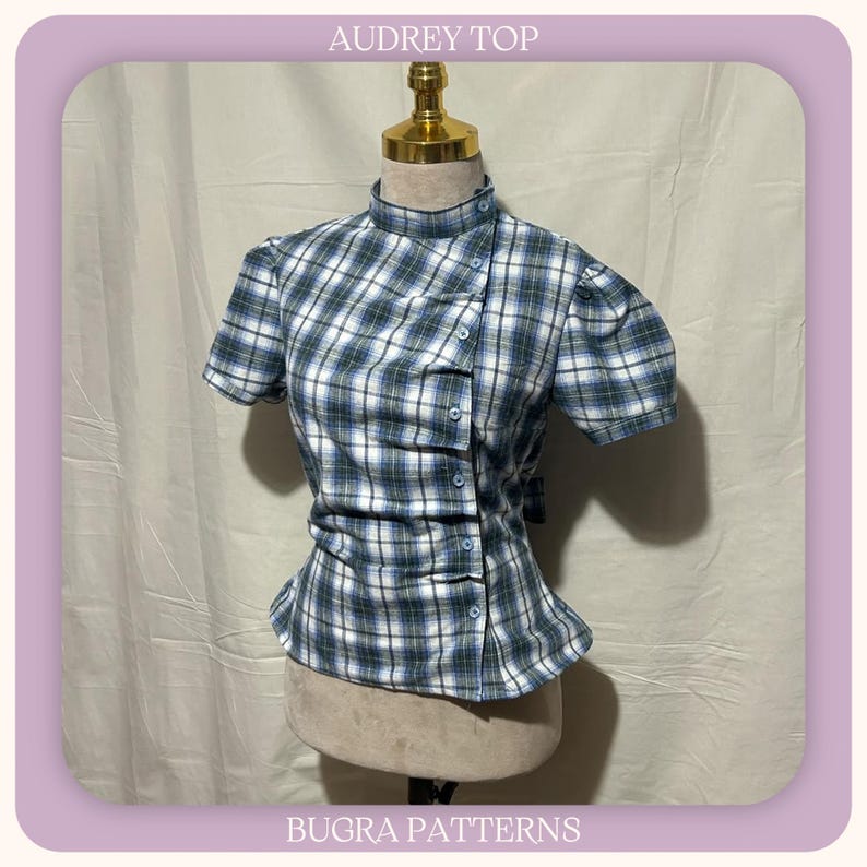 May include: A short-sleeved top with a blue, white, and green plaid pattern, featuring a high collar and an asymmetrical button-down front closure. The garment is displayed on a mannequin and includes the text AUDREY TOP and BUGRA PATTERNS.