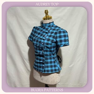 May include: A short-sleeved top with a blue and black plaid pattern, featuring a high collar, a side-buttoned front closure, and a tie-back waist. The text AUDREY TOP and BUGRA PATTERNS is visible at the top and bottom of the image frame.