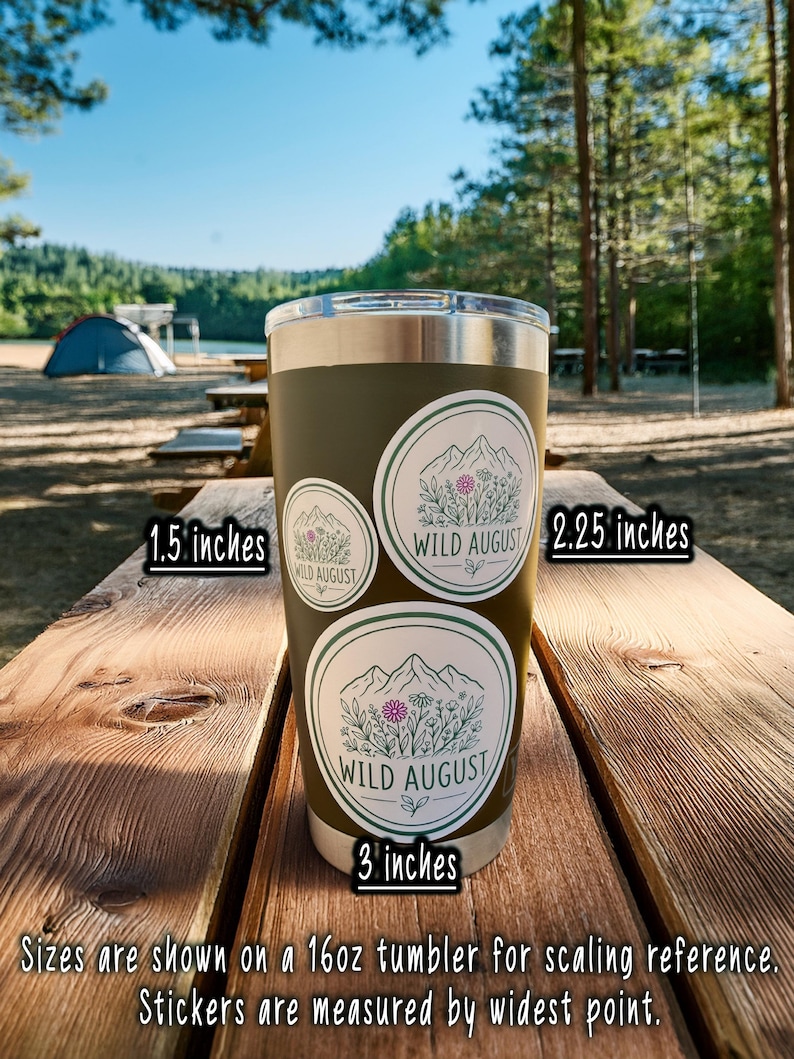 A 16oz tumbler with three stickers on it, placed on a wooden picnic table in a forested area.