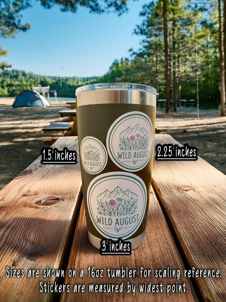 A 16oz tumbler with three stickers on it, placed on a wooden picnic table in a forested area.