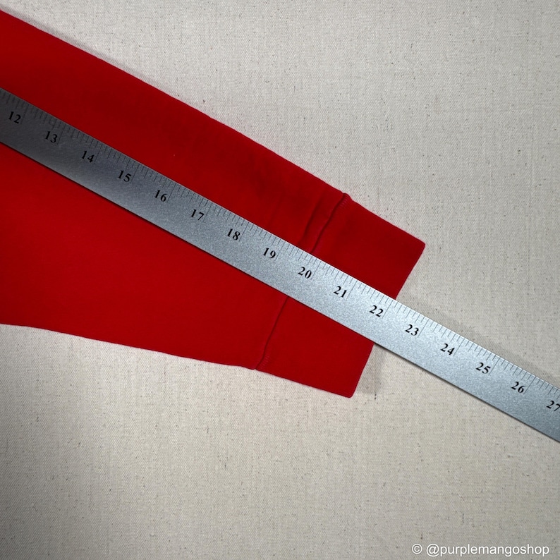 May include: A bright red long-sleeved shirt sleeve with a ruler measuring from 12 to 27 inches. The sleeve is on a neutral background. The text "@purplemangoshop" is visible in the bottom right corner.