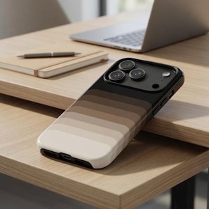 May include: A smartphone case with a gradient design in shades of brown and beige. The case is on a wooden desk, with a laptop and notebook in the background. The case has a black camera module.