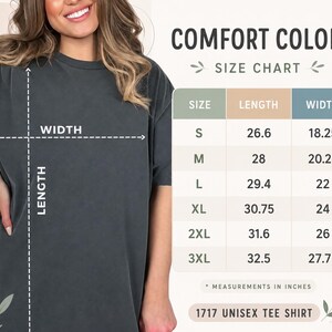 Puede incluir: Una camiseta gris carb&oacute;n de manga corta junto a una tabla de tallas Comfort Colors. La tabla muestra medidas de largo y ancho en pulgadas para las tallas S a 3XL del modelo 1717 unisex tee shirt, con etiquetas claras y texto informativo.