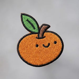 May include: Embroidered orange patch with a smiling face, black outline, and a green leaf. The orange is a vibrant, textured color, and the leaf is a bright green. The patch is likely for clothing or accessories.
