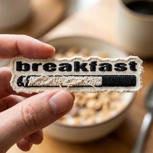 May include: A white ceramic mug with a black handle and the text "But First, Coffee" in a black, handwritten-style font. The mug is on a white surface.