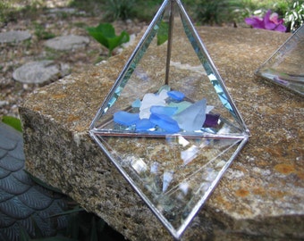 May include: A glass pyramid with a clear base and a silver frame. The pyramid is filled with small pieces of blue and white sea glass.