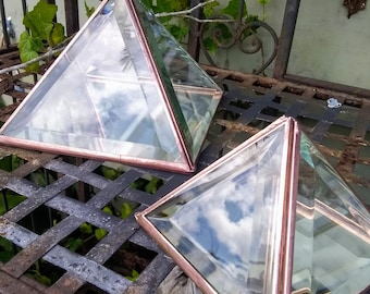 May include: Two glass pyramids with copper trim, reflecting the sky. The pyramids are sitting on a metal grate.