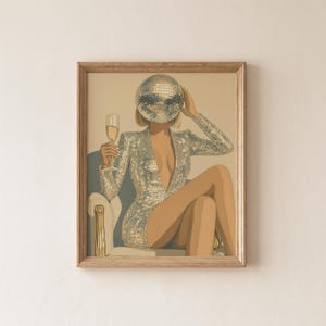 May include: A framed art print depicts a person in a silver sequined dress and a disco ball for a head, holding a champagne glass. The figure is seated in a white chair with gold accents, creating a glamorous, party-themed aesthetic.