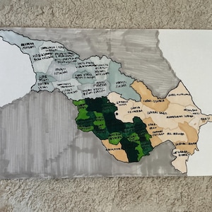 May include: A white ceramic mug with a black handle and the text "But First, Coffee" in a black, handwritten-style font. The mug is on a white surface.