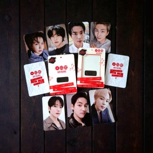 May include: A collection of BTS photo cards and Arirang-branded packaging, arranged on a dark wood surface. The photo cards feature individual members. The packaging is white with red accents and the Arirang logo.
