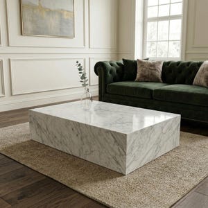 Puede incluir: Una mesa de centro rectangular de mármol con vetas grises se encuentra sobre una alfombra de tonos neutros. La mesa está frente a un sofá de terciopelo verde oscuro con cojines. Un jarrón de cristal transparente con vegetación está sobre la mesa.