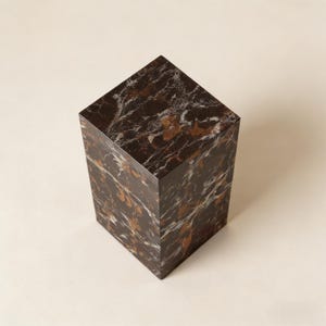 以下が含まれることがあります： 白と金色の縞模様が入った濃い茶色の大理石の台座。長方形のブロックは、装飾品を展示するのに最適な、しっかりとした幾何学的な形状をしています。表面は光を反射する研磨仕上げです。