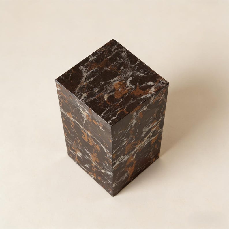 以下が含まれることがあります： 白と金色の縞模様が入った濃い茶色の大理石の台座。長方形のブロックは、装飾品を展示するのに最適な、しっかりとした幾何学的な形状をしています。表面は光を反射する研磨仕上げです。