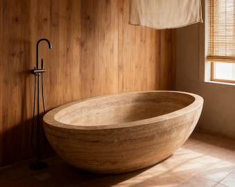 May include: A large, oval-shaped stone bathtub with a natural, earthy color palette. The tub is the focal point, set against a backdrop of wooden paneling and a black faucet. The bathroom has a spa-like atmosphere.