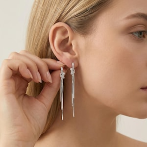 Puede incluir: Pendientes colgantes plateados con diseño de nudo y múltiples hebras. Los pendientes tienen pequeños detalles brillantes. Los pendientes son una joya.