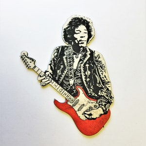 May include: Wooden cutout of a musician with a guitar. The figure is in black and white, with a red guitar. The musician is wearing a jacket with a detailed pattern. The guitar has a white pickguard.