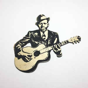 May include: Black and white silhouette of a person playing a guitar. The person is wearing a hat and a suit. The guitar is a wooden acoustic guitar.
