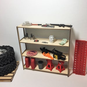 May include: A wooden shelf unit with four shelves, filled with various miniature tools and accessories. The shelves are made of light brown wood and the unit is standing on a white surface. The items on the shelves include a chainsaw, a pair of car jacks, a red and white Jeep logo, a pair of red gas cans, a white helmet, and a black rifle.